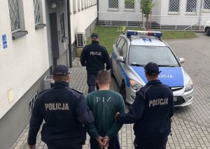 trzej policjanci prowadzą zatrzymanego mężczyznę w tle radiowóz policyjny
