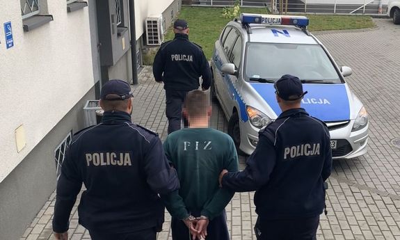 trzej policjanci prowadzą zatrzymanego mężczyznę w tle radiowóz policyjny