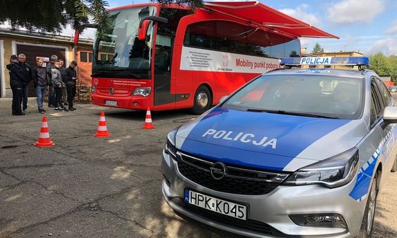 Na zdjęciu widnieje radiowóz wraz z autobusm do oddawania krwi w tle