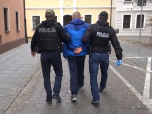 Na zdjęciu widnieje zatrzymany w eskorcie dwóch policjantów