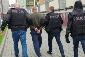 Na zdjęciu znajduje się zatrzymany w eskorcie dwóch policjantów.