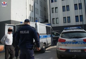 41-letni mężczyzna podejrzany o pozbawienie wolności kobiety oraz policjanci, w tle radiowozy