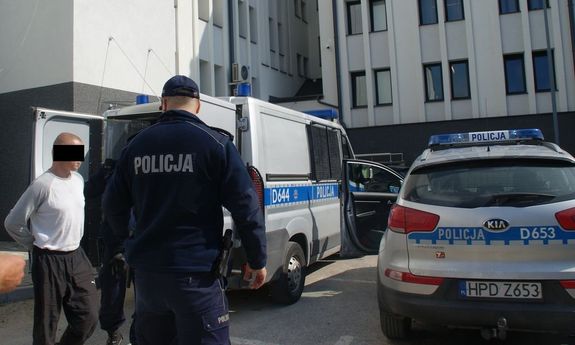 41-letni mężczyzna podejrzany o pozbawienie wolności kobiety oraz policjanci, w tle radiowozy