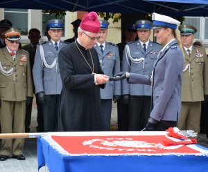 na zdjęciu obok sztandaru jest biskup oraz policjantka