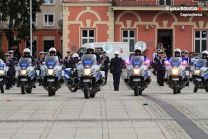 Policjanci na motorach w szyku, za nimi orkiestra honorowa policji