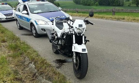 zaparkowany na poboczu motocykl za nim stoją dwa radiowozy policyjne