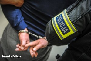 policjant prowadzi zatrzymanego mężczyznę w kajdankach