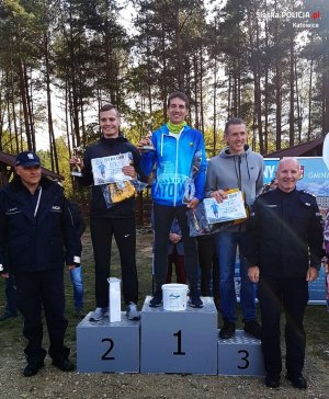 trzech najlepszych zawodników na podium po bokach stoją dwaj policjanci