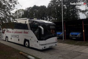 Mobilna stacja Regionalnego Centrum Krwiodawstwa i Krwiolecznictwa w Katowicach stoi na policyjnym parkingu, w tle stoją zaparkowane policyjne busy.