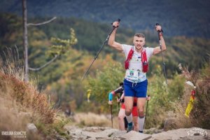 Tomasz Czernek na trasie biegu Beskidy Ultra Trail. Mężczyzna biegnie z kijkami, w tle góry