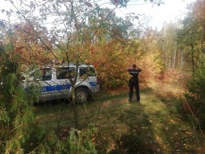 radiowóz policyjny  stojący w lesie oraz policjant w trakcie poszukiwań