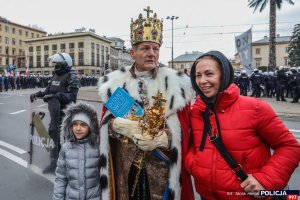 kobieta, dziecko oraz mężczyzna przebrany za króla w tle policjanci