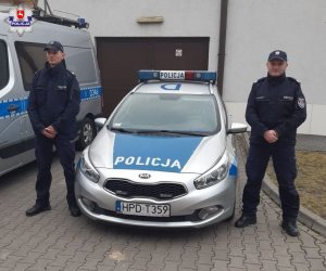 dwaj policjanci stoją przy radiowozie