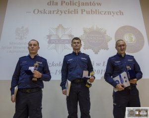 trzech najlepszych policjantów stoi na podium trzymając dyplomy i statuetki