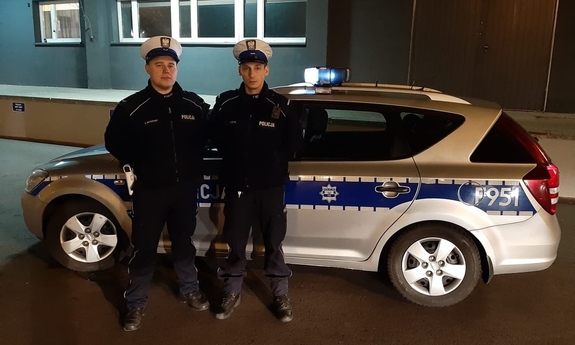 dwaj policjanci stoją przy radiowozie