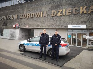 policjant i policjantka stoją przy radiowozie