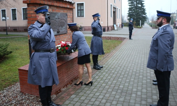 policjantka i policjanci składają wiązankę kwiatów pod tablicą