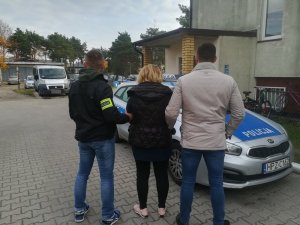 Zatrzymana kobieta w sprawie oszustwa, w eskorcie dwóch policjantów