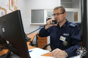 Policjant siedzący przed komputerem rozmawiający przez  telefon