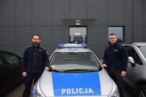 Policjanci którzy eskortowali pacjenta do szpitala stoją przy radiowozie