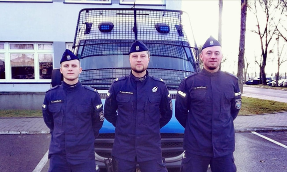 trzej policjanci stoją przed radiowozem