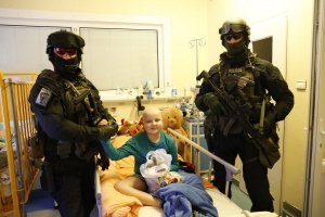 Policjanci i kontrterroryści z prezentami u małych pacjentów - dwóch policjantów stoi przy łóżku chorego chłopca