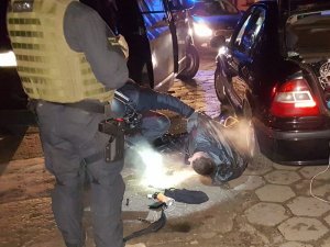 zatrzymany mężczyzna leży skuty w kajdankach na ziemi obok stoją samochody i policjanci