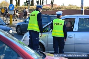 policjanci ruchu drogowego podczas rozmowy z kierującym stoją przy zatrzymanym do kontroli drogowej samochodzie