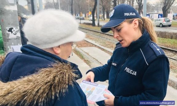 Policjantka przekazuje ulotkę informacyjną mieszkance Wrocławia na przestanku tramwajowym