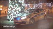 oznakowany radiowóz policyjny z włączonymi sygnałami świetlnymi stoi przed choinką świąteczną