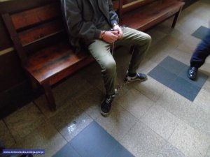 podejrzany w kajdankach siedzi na ławce czekając przed salą