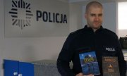 Starszy sierżant Mariusz Brzezina stoi na tle napisu Policja ze swoimi książkami