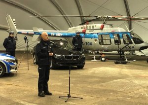 Komendant Główny Policji przed mikrofonem, z tyłu sprzęt zakupiony w 2019 roku - śmigłowiec Bell-407 i nieoznakowane bmw