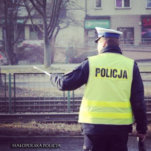 policjant ruchu drogowego w kamizelce odblaskowej z napisem &quot;Policja&quot; podczas zatrzymywania pojazdu do kontroli