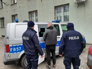 umundurowani policjanci prowadzą zatrzymanego który wsiada do oznakowanego radiowozu