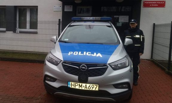 Policjantka stoi przy radiowozie na tle posterunku