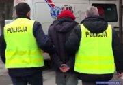 policjanci w kamizelkach odblaskowych z napisem &quot;POLICJA&quot; prowadzą zatrzymanego