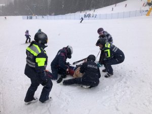 Umundurowani policjanci udzielają pomocy osobie na stoku.