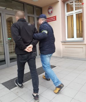policjant prowadzi zatrzymanego, wchodzą do Prokuratury Rejonowej w Tarnowskich Górach&quot;&gt;