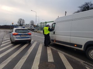 Policjant stoi przy samochodzie i za pomoca alkomatu bada trzeźwość kierowcy