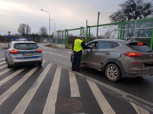 Policjant stoi przy samochodzie i za pomoca alkomatu bada trzeźwość kierowcy