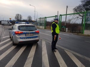 Policjnat stoi przy radiowozie z alkomatem i policyjnym lizakiem w recę