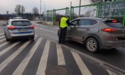 Policjant stoi przy samochodzie i za pomoca alkomatu bada trzeźwość kierowcy