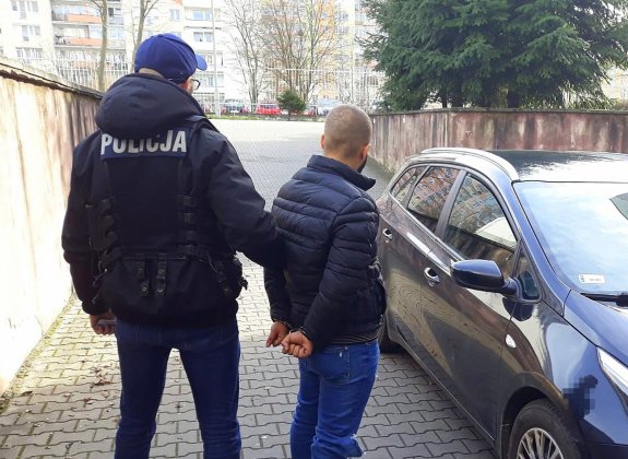 umundurowany policjant stoi z zatrzymanym przy radiowozie