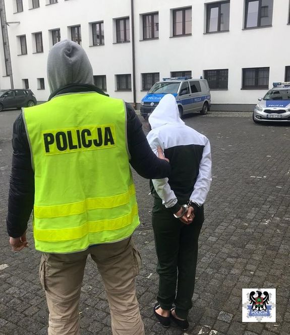 policjant w kamizelce odblaskowej z napisem policja stoi z zatrzymaną oszustką