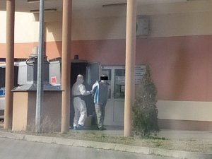Mężczyzna prowadzony przez funkcjonariusza w kombinezonie ochronnym