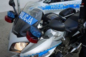Policyjny motor, a w tle radiowóz.&quot;&gt;