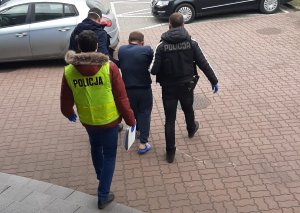 Policjanci prowadzą zatrzymanego do samochodu