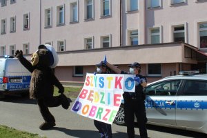 policyjny miś przy radiowozie i policjantki z plakatem „Wszystko będzie dobrze”