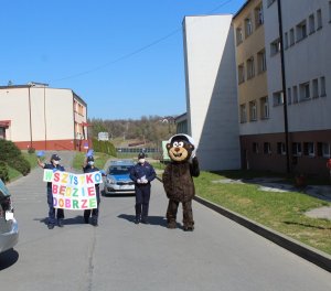 policyjny miś przy radiowozie i policjantki z plakatem „Wszystko będzie dobrze”